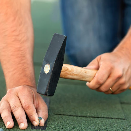 Roofer nails in shingles.