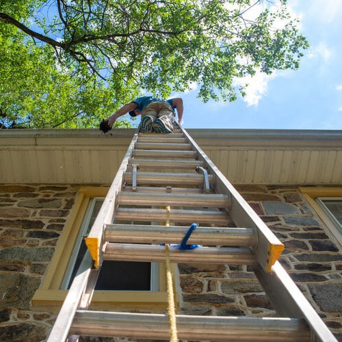 view from below of a worker installing gutters along a roof